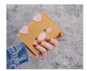 Detailed view of yellow cartoon pig mini leather wallet held in hand showing texture