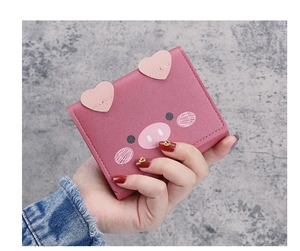 Close-up of pink cartoon pig leather wallet with heart ears held by a hand