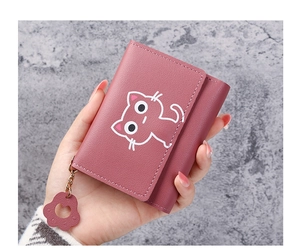 Detail of a pink trifold wallet featuring a cat motif and a leather paw charm in hand