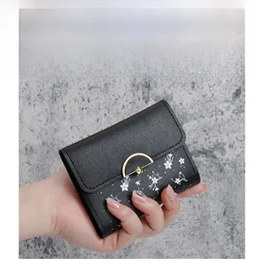Close-up of a floral print mini wallet with a gold semi-circular clasp held by a hand