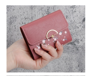 Close-up of pink tri-fold wallet featuring floral print and golden metal buckle