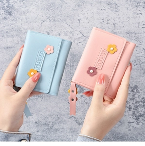 Détail de portefeuilles en cuir rose et bleu avec breloques fleurs perlées et zips