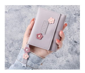 Gros plan du portefeuille en cuir lavande avec breloques florales tenu à la main