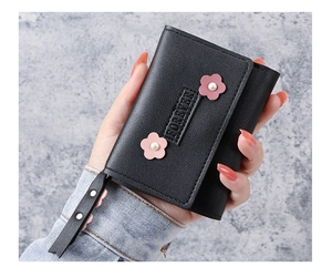Gros plan du portefeuille noir avec fleurs roses et perle, tenu à la main par une femme