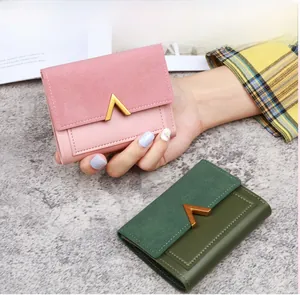 Detail of pink and dark green tri-fold wallets featuring matte suede texture and gold V-clasp
