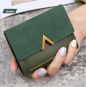 Detail of green tri-fold faux leather wallet with gold V-metal clasp held by a hand