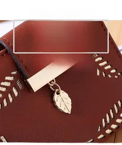 Detail of laser-cut leaf patterns and gold metal leaf pendant on brown PU leather wallet