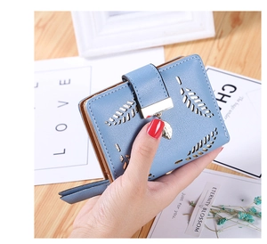 Detail of light blue leather wallet featuring laser-cut leaf pattern and metal pendant
