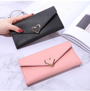 Detail of long envelope wallet with golden heart buckle on marble background with accessories