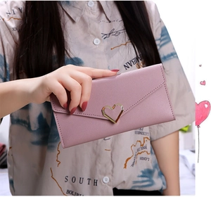 Close-up of a pink long envelope wallet featuring a gold heart buckle held by a model