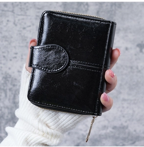 Close-up of black glossy oil wax leather wallet with snap buckle and gold zipper detail