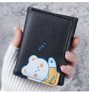 Detail of hand-held black trifold wallet featuring a cute 'Hey Bear' cartoon pattern