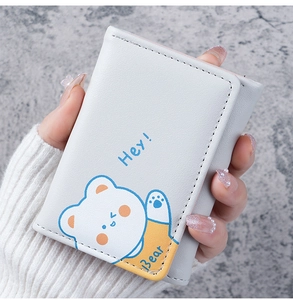 Close-up of a compact tri-fold cream wallet with a cute blue bear design and Hey Bear text