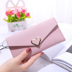 Elegant long pink envelope wallet with heart buckle held against a soft floral background