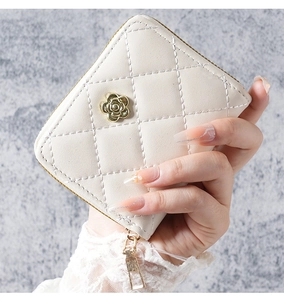 Detail of beige quilted wristlet wallet with gold camellia accent and metallic zipper