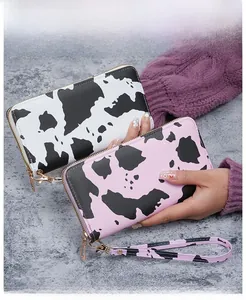Close-up of long zip-around wallets featuring black and pink cow print patterns with wristlet