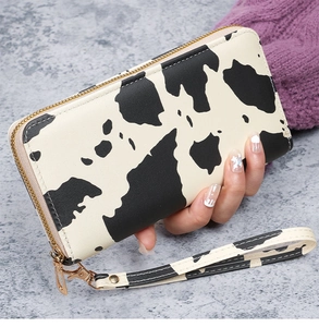 Detail of a zip-around wallet featuring cow print pattern and gold hardware with wristlet