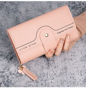 Detail of pink long trifold wallet featuring tassel pendant and gold clasp held by a hand