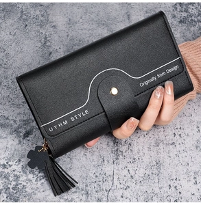 Detailed view of women's long black tri-fold wallet with lychee leather texture and tassel