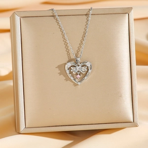 Elegant heart pendant necklace with pink gem and silver bow on gold jewelry box display