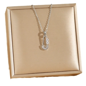 Silver titanium necklace with zircon-encrusted safety pin pendant on gold jewelry box