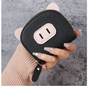 Handheld view of a mini black pig coin purse featuring pink ears and a gold zipper