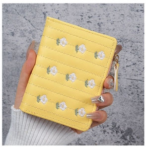 Close-up of yellow embroidered wallet featuring small white daisy patterns and a gold zipper