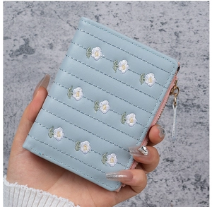 Detail of light blue embroidered daisy wallet with gold zipper in a hand-held shot