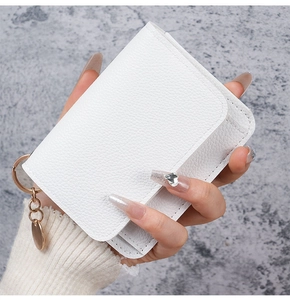 Close-up of white lychee texture leather wallet with gold keychain and round charm