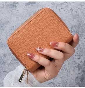 Close-up of orange-brown litchi grain leather card holder with gold zippers held by a hand