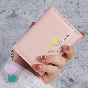 Gros plan d'un portefeuille rose à trois volets avec motif tulipe et pendentif