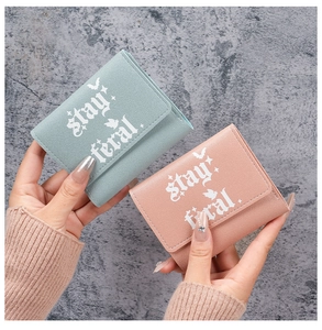 Close-up of pink and green trifold wallets with stay feral text and bat motifs