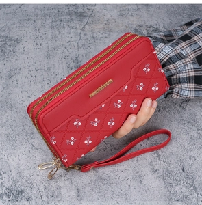 Detail of red quilted faux leather long wallet with floral print and wrist strap