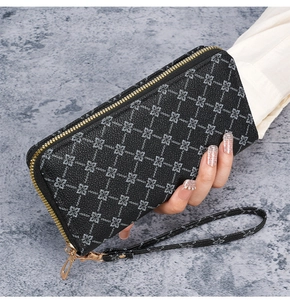 Detail of long black zip wallet featuring silver floral patterns and gold wrist strap