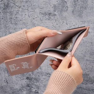 Pink PU leather tri-fold wallet with Stay feral text held against a grey background