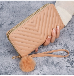 Detail of peach pink V-quilted clutch with dual zippers and fluffy pompom charm decor