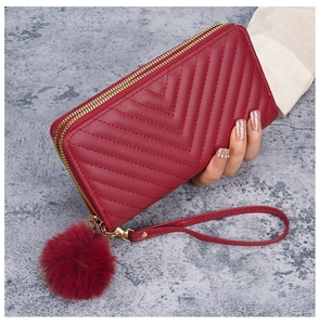Detail of red quilted long wallet with double zippers, wristlet and pompom charm