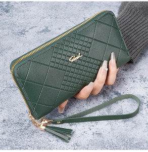 Détail d'un portefeuille long en similicuir matelassé vert foncé avec pompon et zip doré