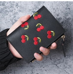Close-up of litchi leather wallet featuring red cherry embroidery and golden zipper detail