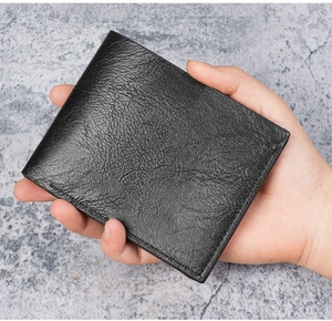 Man holding black lychee grain leather bifold wallet to show compact size and texture