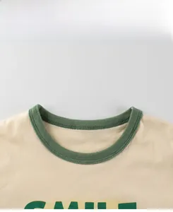 Gros plan sur le col côtelé vert et l'imprimé SMILE sur le t-shirt en coton pour enfants