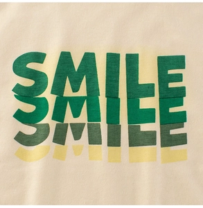 Détail du tissu en coton avec un imprimé graphique SMILE coloré sur le t-shirt enfant