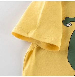 Close-up of sleeve stitching on yellow cotton kids' T-shirt with green dinosaur print