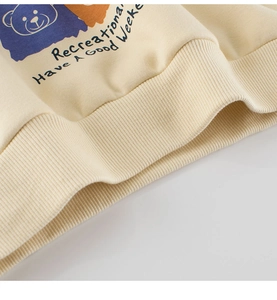 Detailed close-up of cream knit sweatshirt hem showing ribbed cuffs and cartoon bear print