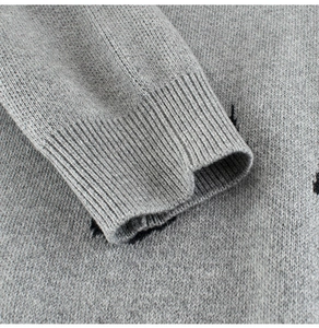 Détail rapproché des poignets côtelés et des coutures fines d'un pull gris en tricot