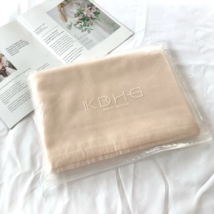 Detailed view of beige cashmere feel scarf in branded zipper bag packaging