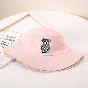 Détail du chapeau bob en coton rose avec un écusson d'ours à carreaux noir et blanc