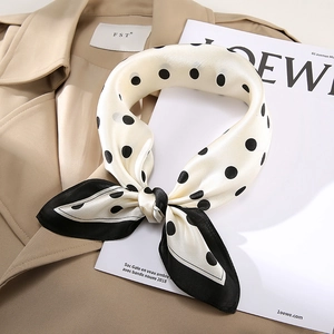 Detailed close-up of a knotted silk scarf with black polka dots on cream background