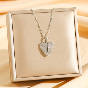 Elegante collar con colgante de corazón y ala con circonitas sobre fondo de joyero dorado