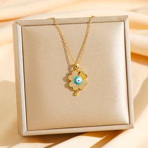 Golden clover necklace with evil eye charm and zircon inlay on silk background